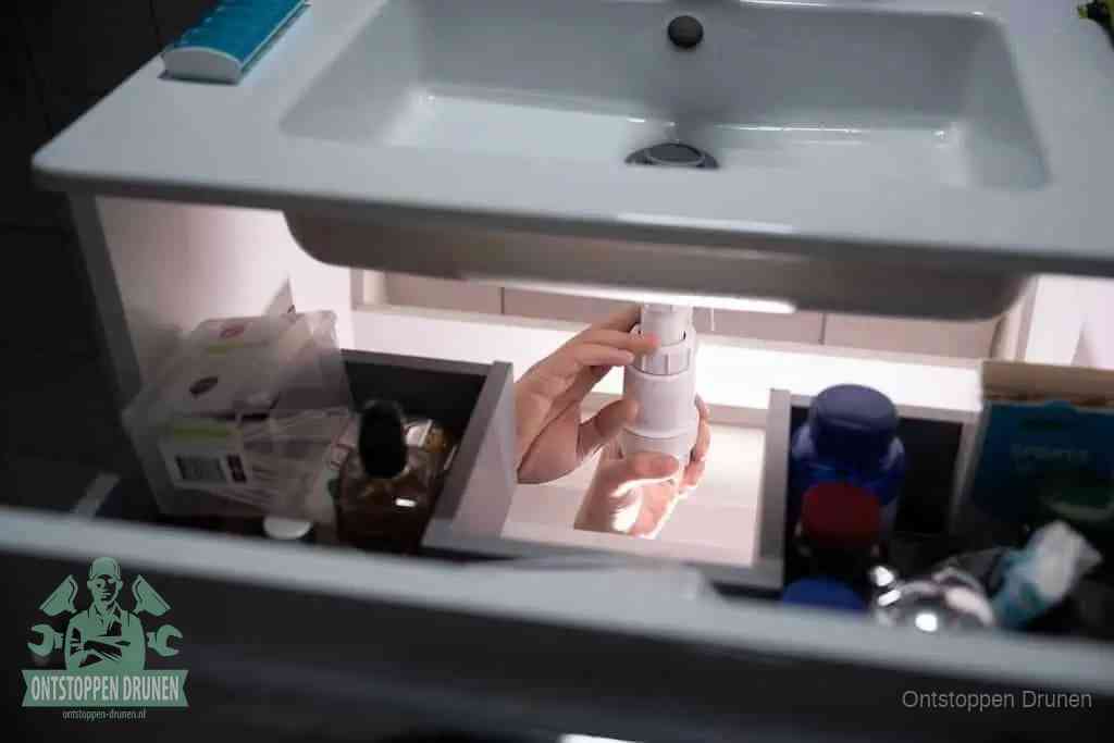 Een pompfles met zeep boven een wastafel, de heet water en afwasmiddel-methode om een vetprop in de afvoer los te maken in Drunen