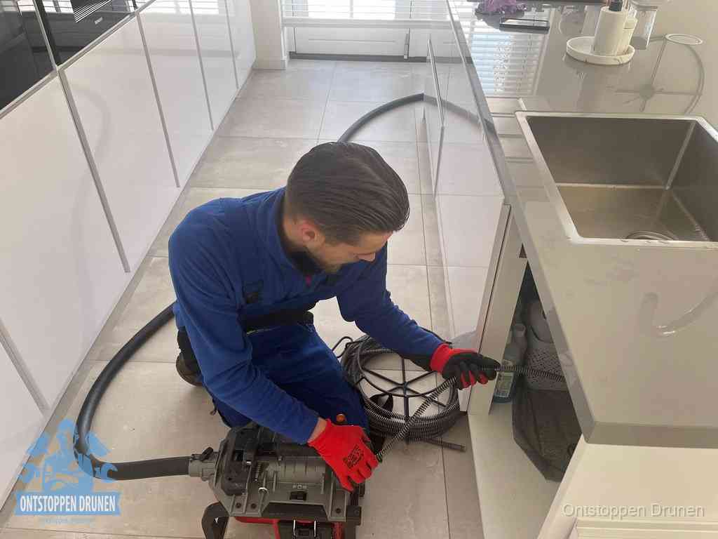 Een monteur ontstopt de keukenafvoer onder de spoelbak met een elektrische veermachine in Drunen