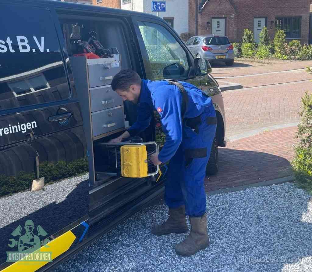 Een monteur pakt buiten op de oprit gereedschap uit de bedrijfsbus, het moment om een professional in te schakelen voor een verstopte afvoer in Drunen