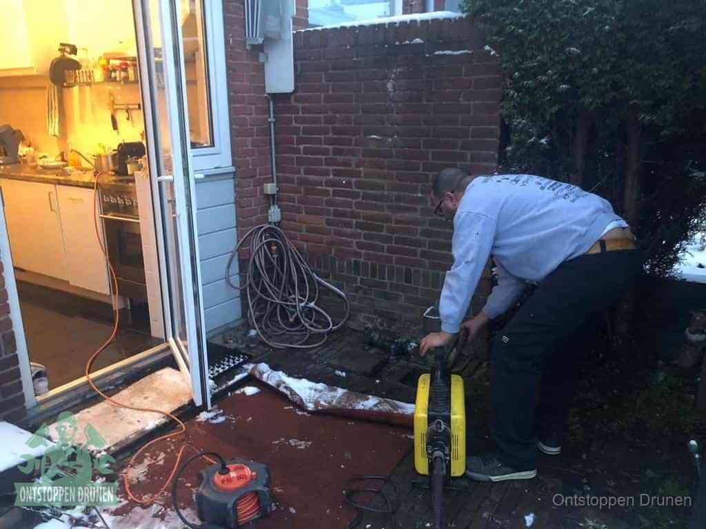 Een monteur werkt buiten bij een open riool-/grondput met een elektrische ontstoppingsmachine om een verborgen afvoerprobleem op te sporen in Drunen