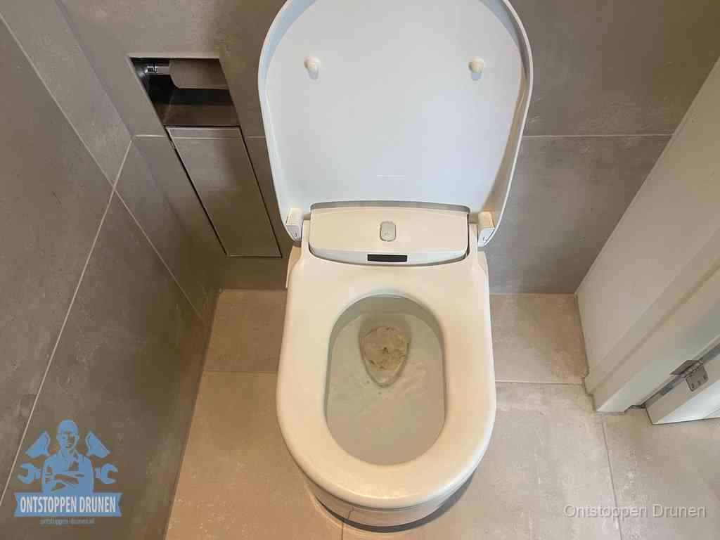 Een wit hangtoilet waarin een prop wc-papier op het water blijft drijven, een duidelijk signaal van een verstopte wc in Drunen