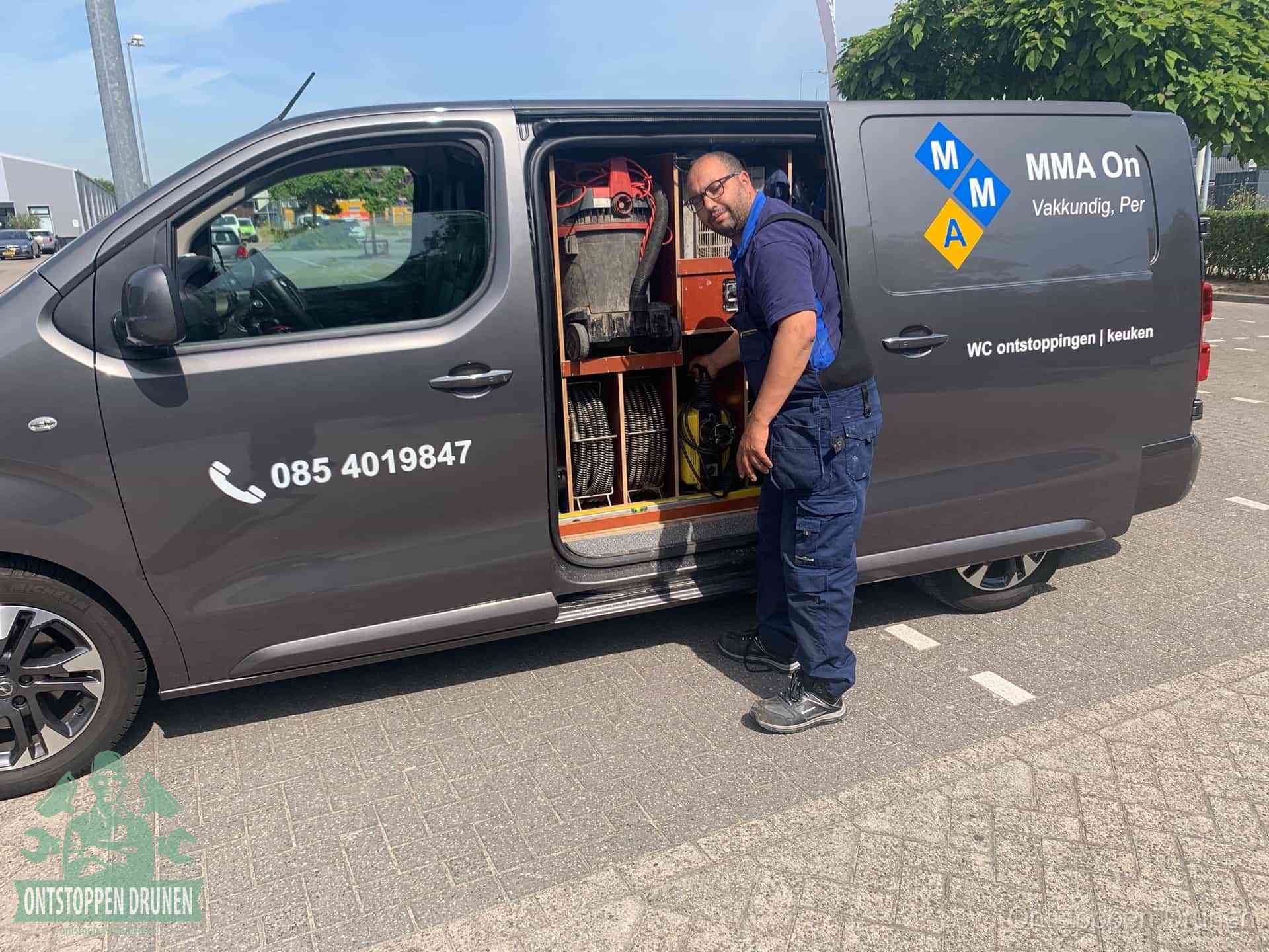 Een monteur bij de open schuifdeur van zijn bedrijfsbus op een parkeerplaats, klaar om de oorzaak van terugkerende afvoerverstoppingen aan te pakken in Drunen