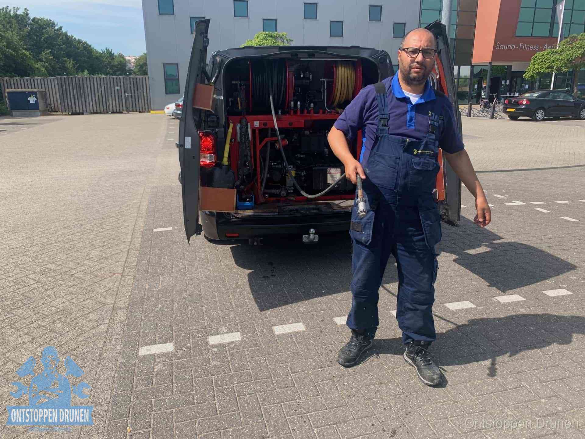 Een monteur bij zijn bestelbus met een hogedruk- en rioolreinigingsunit, klaar om de oorzaak van terugkerende wc-verstoppingen aan te pakken in Drunen