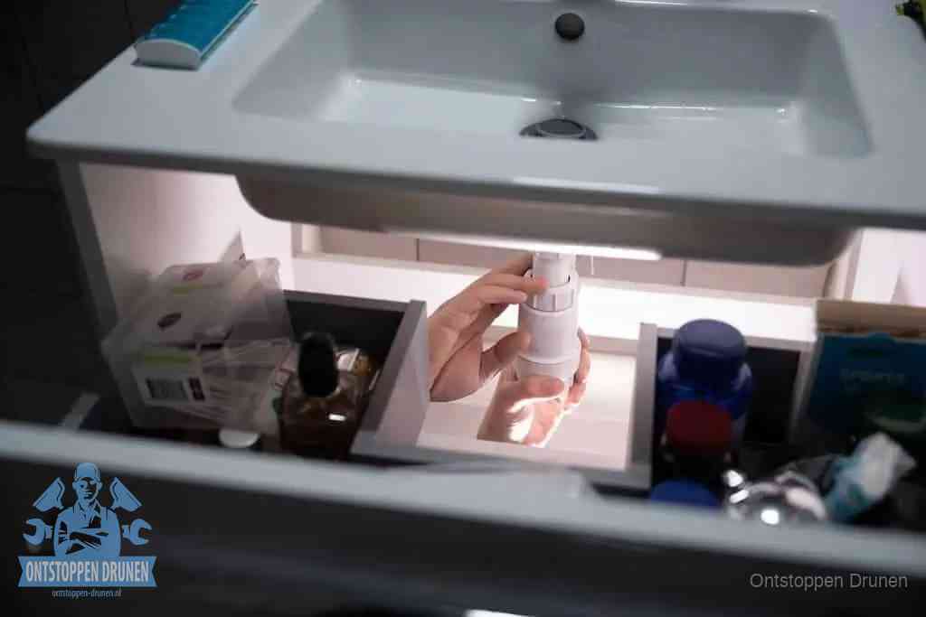 Een pompfles met zeep boven een wastafel in de toiletruimte, de warm water en afwasmiddel-methode om de wc te ontstoppen in Drunen